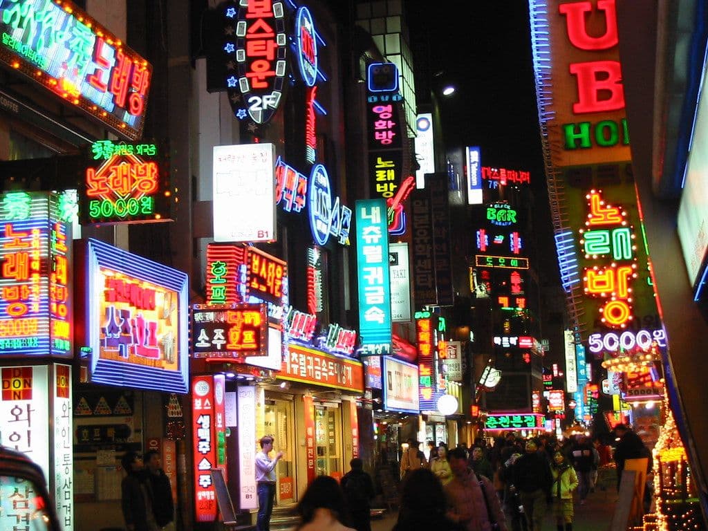 A Seoul side street at night, crowded and lit wall-to-wall with neon signs