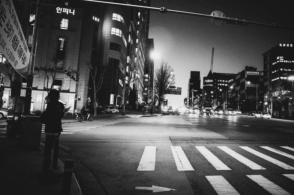A person waiting alone at a crosswalk on a Seoul street at night